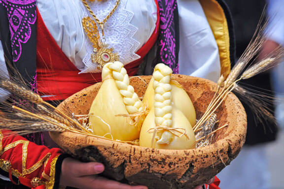 sardischer Zopfkäse in Holzkorb getragen von einer Frau in traditionellem Kleid